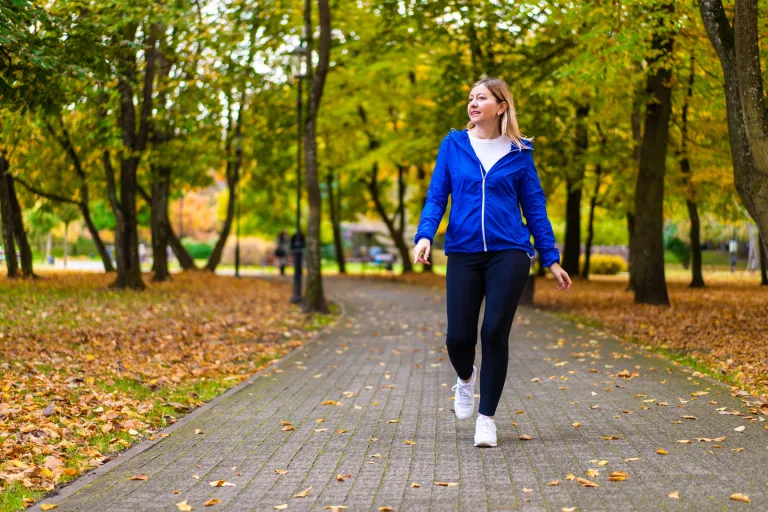 Jeune femme en veste bleue marchant dans un parc aux feuilles d’automne