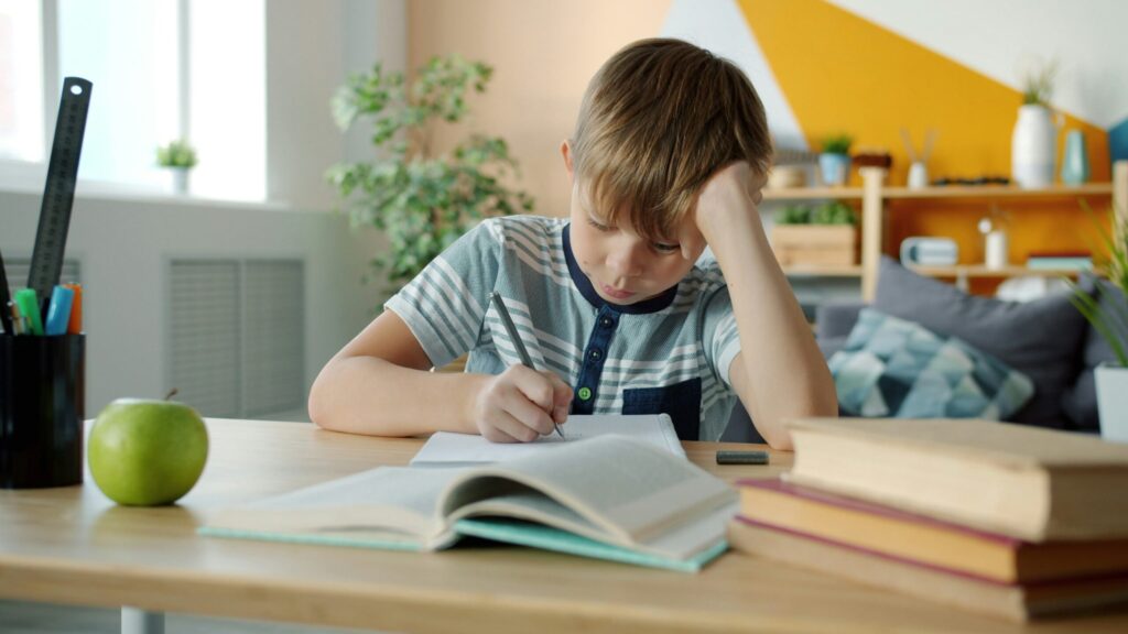 Garçon pensif qui fait ses devoirs à un bureau, entouré de livres