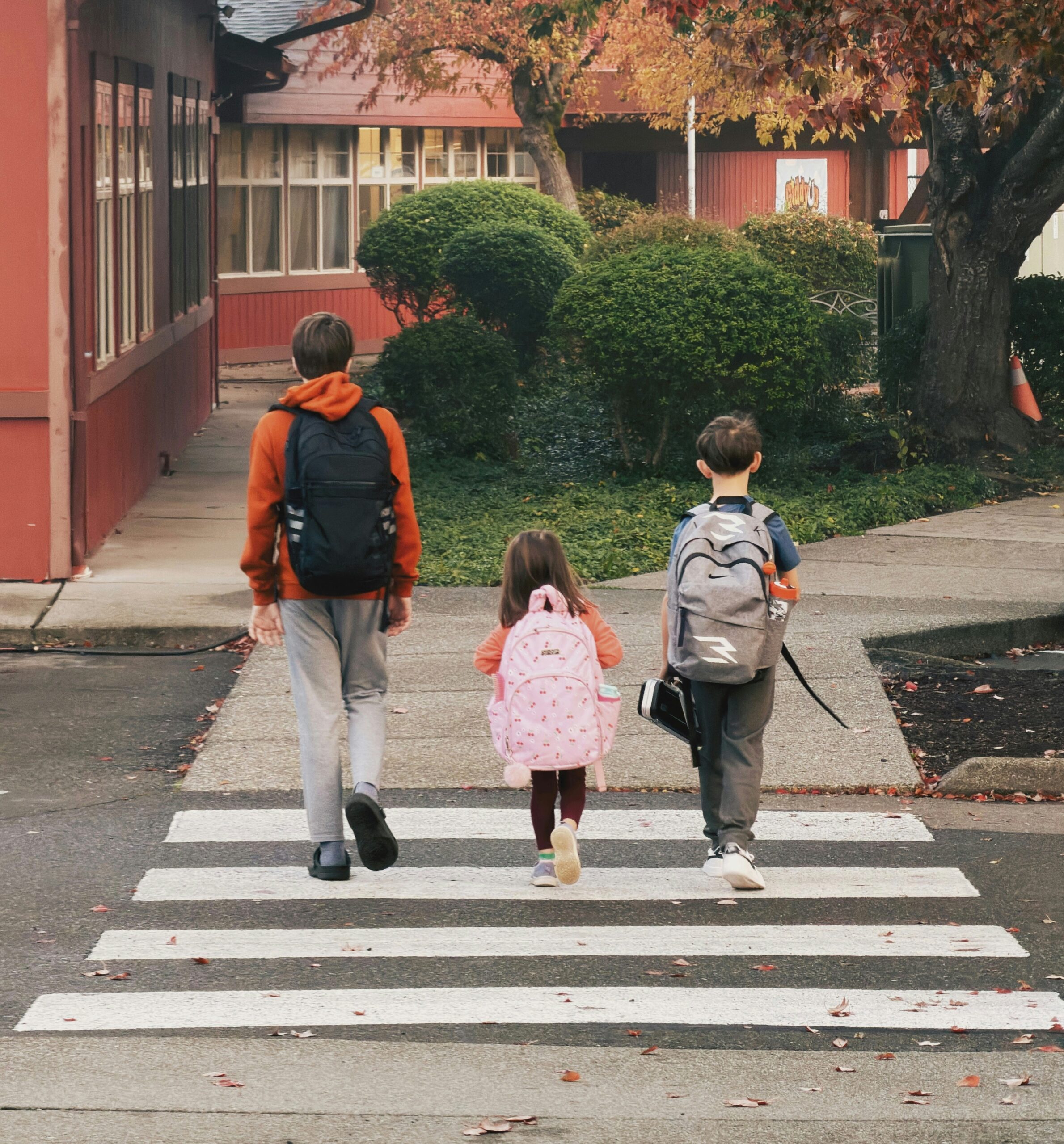 Trois enfants avec sacs à dos traversant un passage piéton devant l’école