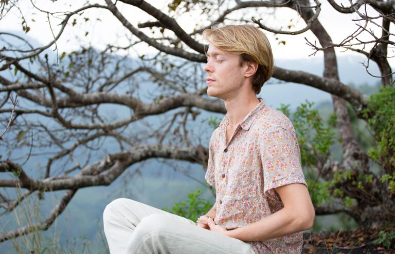 Jeune homme méditant les yeux fermés, assis en pleine nature