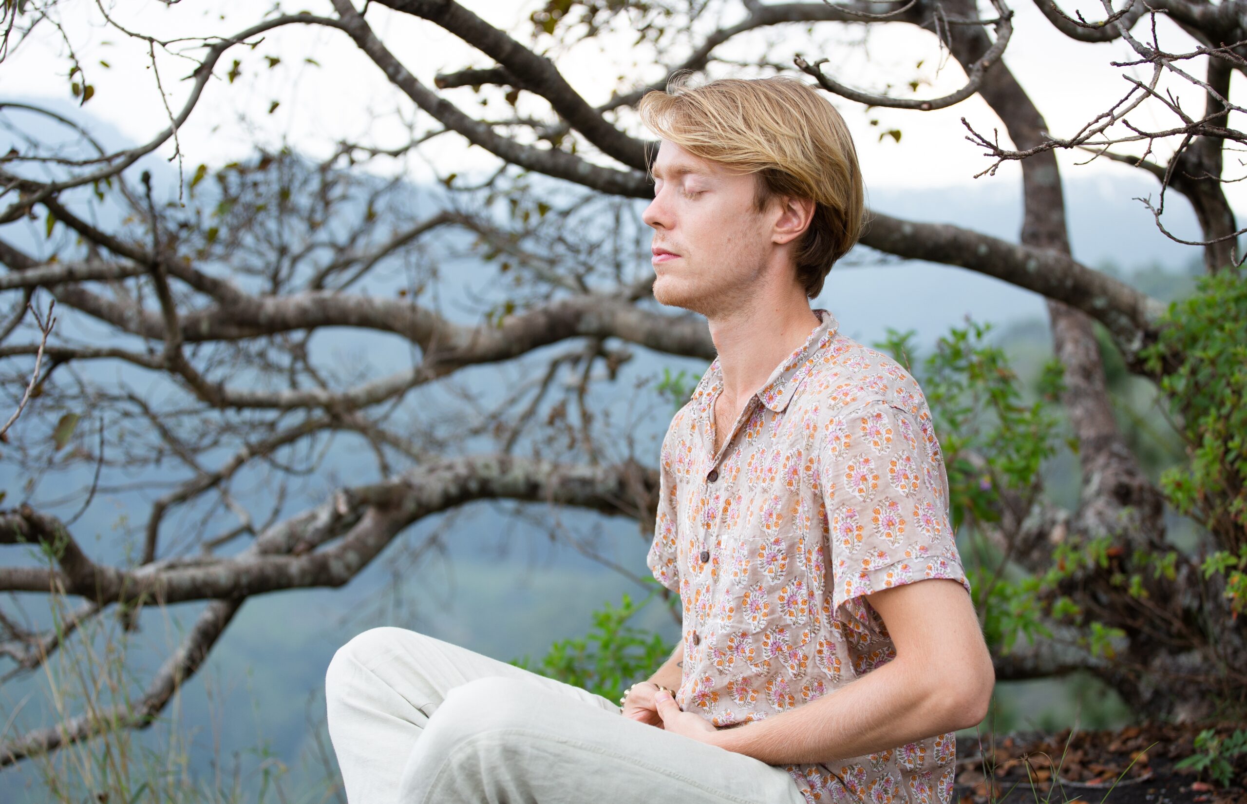 Jeune homme méditant les yeux fermés, assis en pleine nature