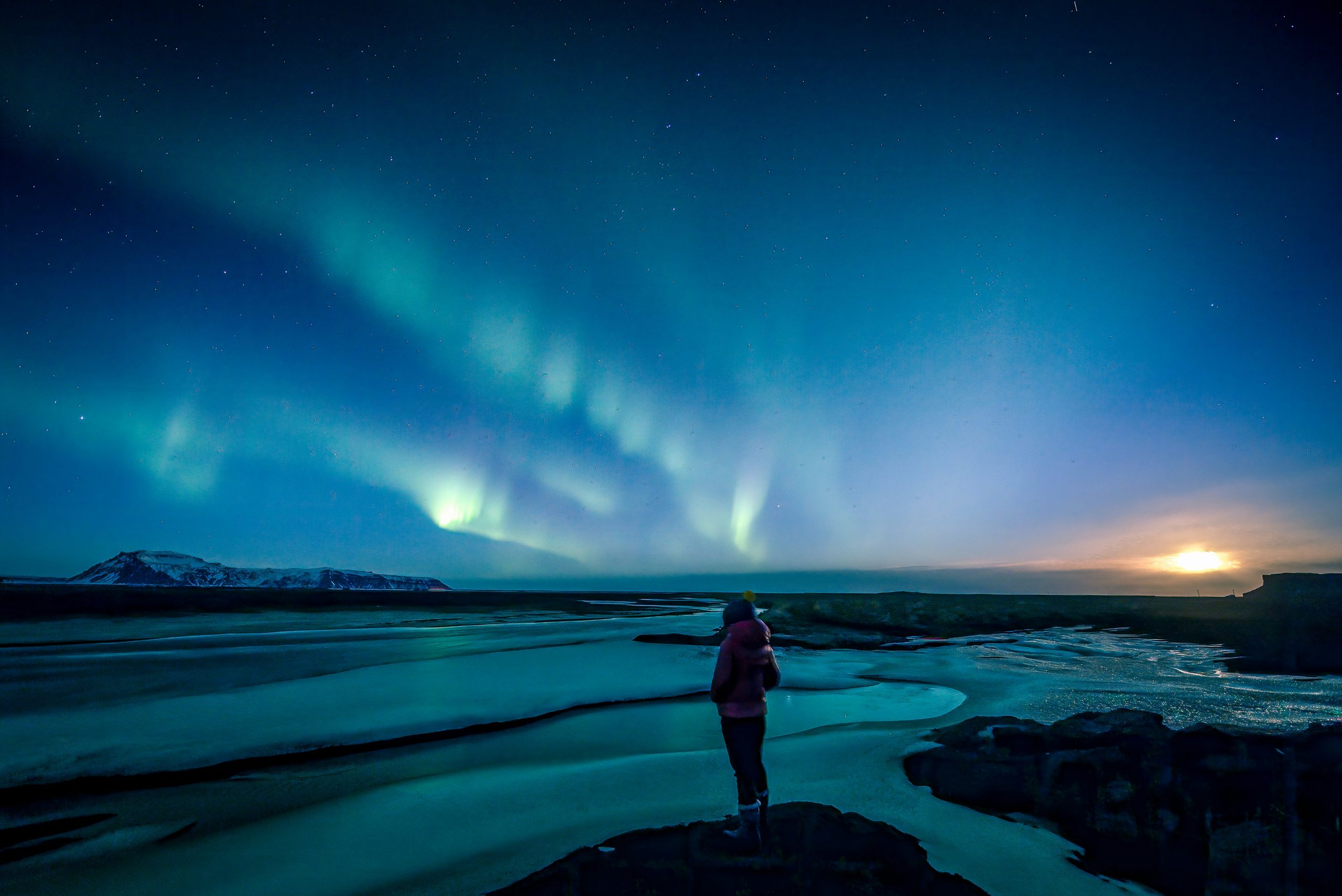 Personne seule de dos contemplant une aurore boréale au-dessus d’un paysage nocturne