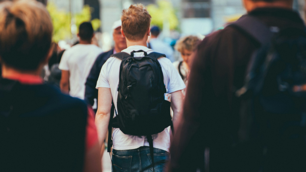 Un jeune avec un sac à dos marche au milieu d’une foule